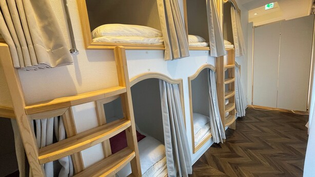 Bunk beds with wooden frames and curtains, a wooden herringbone floor, and a door with an exit sign. - 54 Journey Tokyo Akasaka (Tokyo)