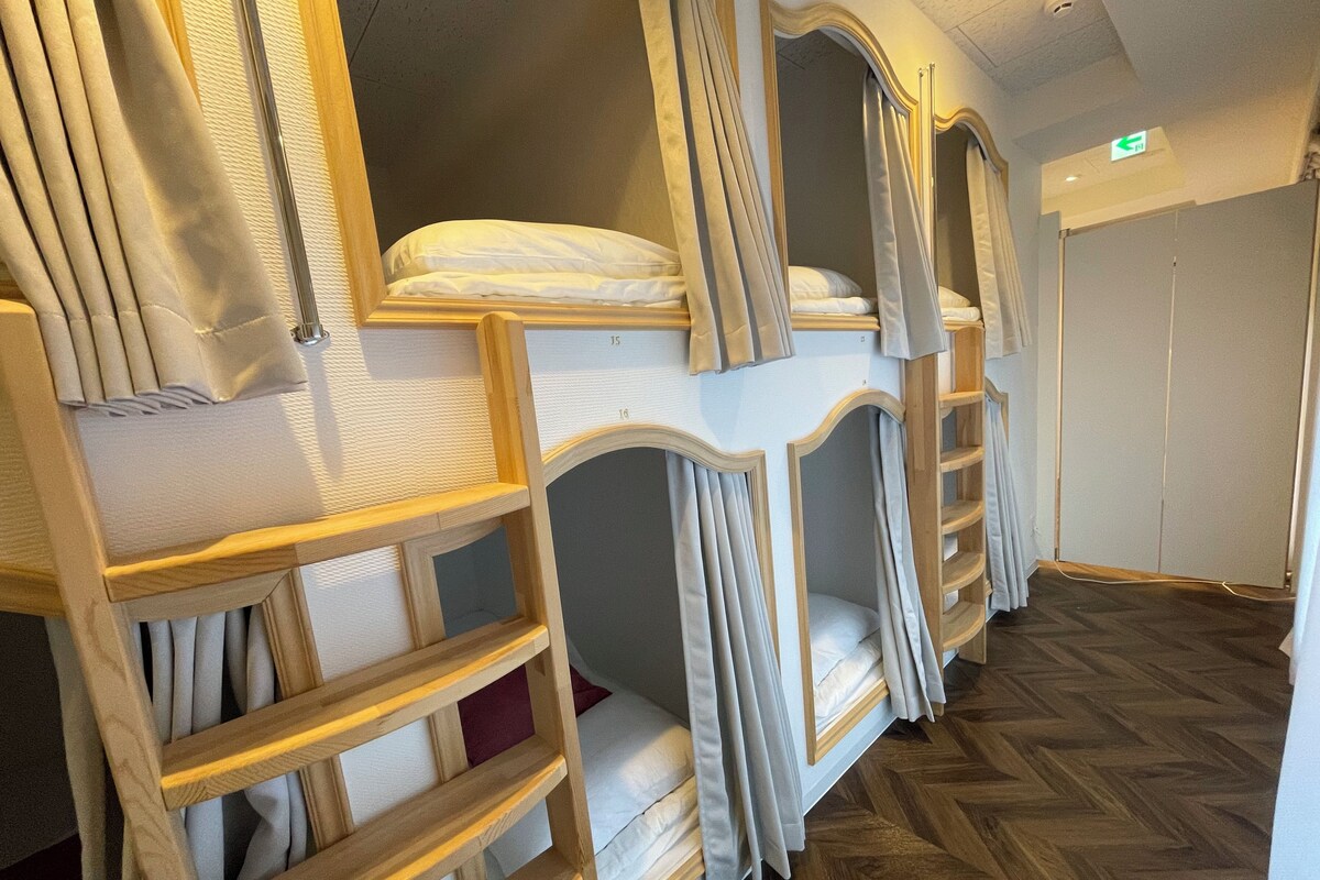 Bunk beds with wooden frames and curtains, a wooden herringbone floor, and a door with an exit sign.