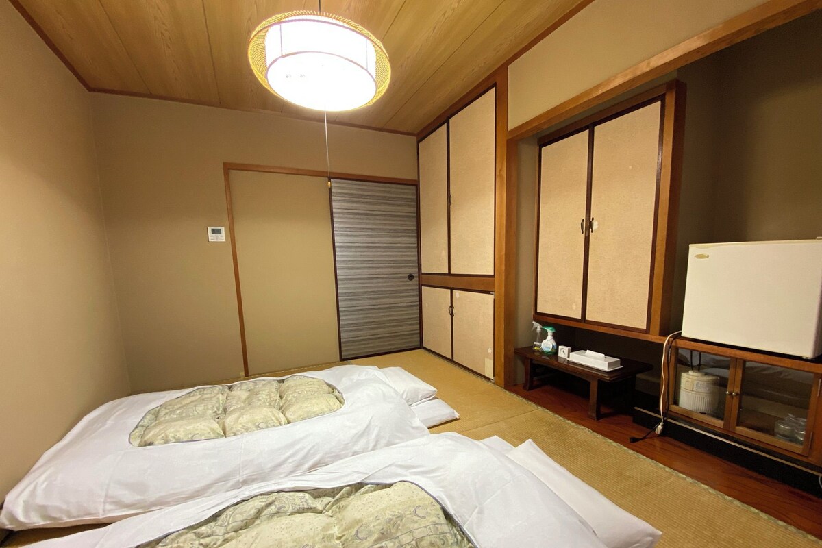 A hotel room with two beds, a wardrobe, a refrigerator, and a ceiling light.