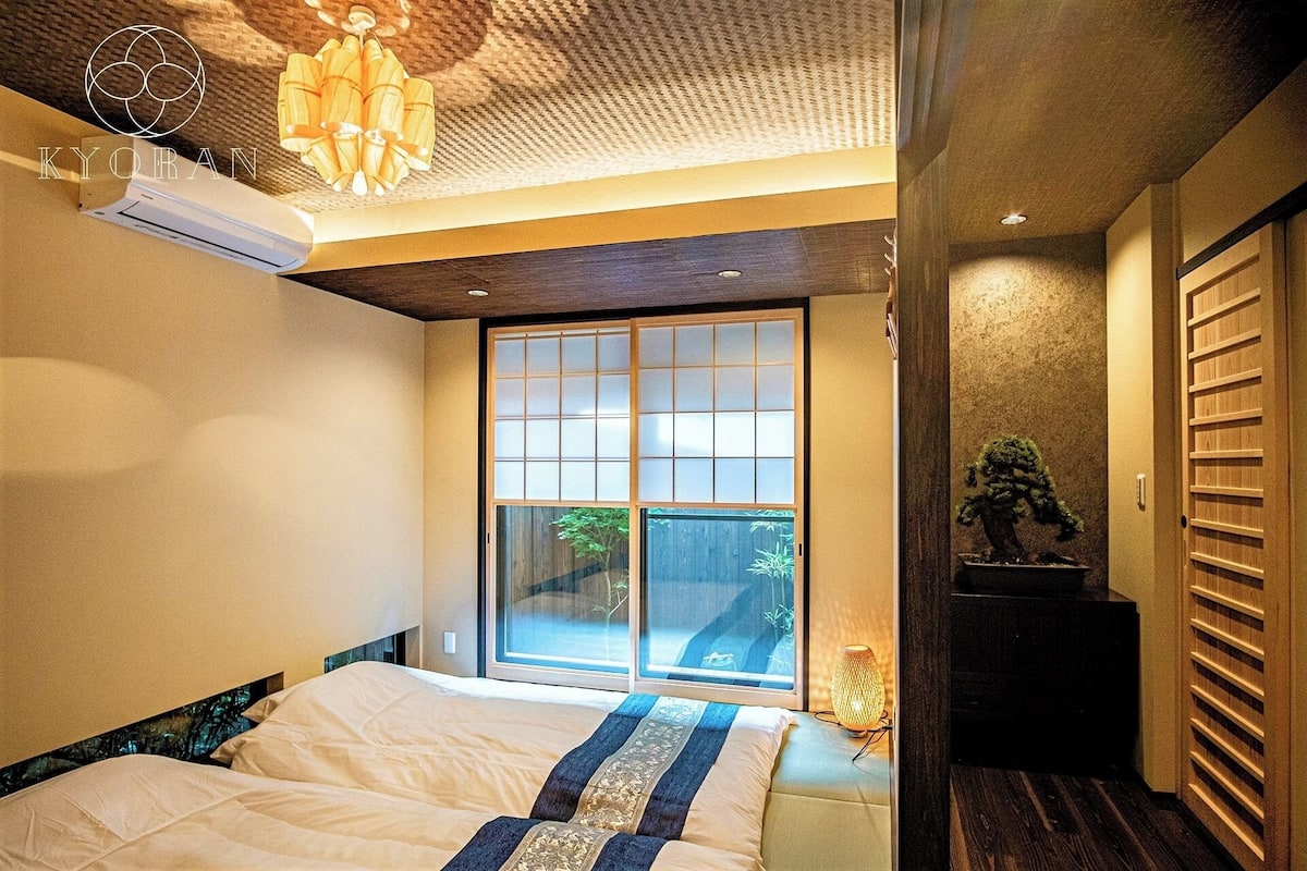 Ein Schlafzimmer mit Bett, Fenster, Pflanze und Deckenventilator.