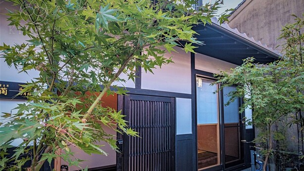 A traditional Japanese building with a sliding door, a small garden area with rocks, and a tree with green leaves. - Kyoran-gengetsu (Kyoto)