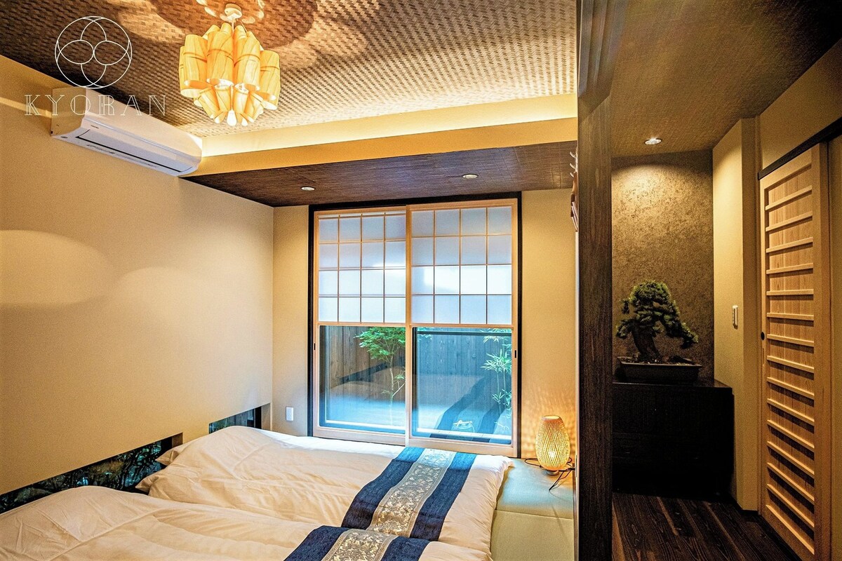 A bedroom with a bed, a window, a plant, and a ceiling fan.