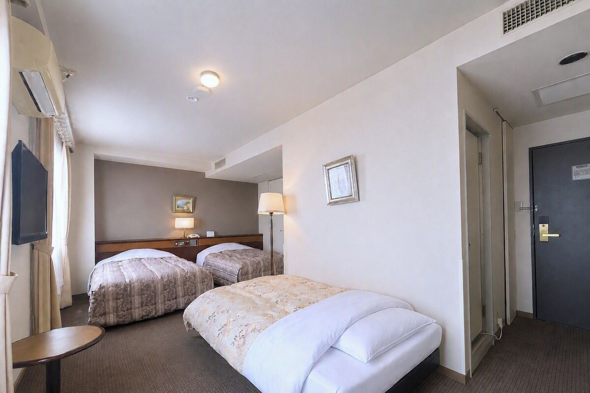 A hotel room with two beds, a flat-screen TV, a bedside table, and a door.