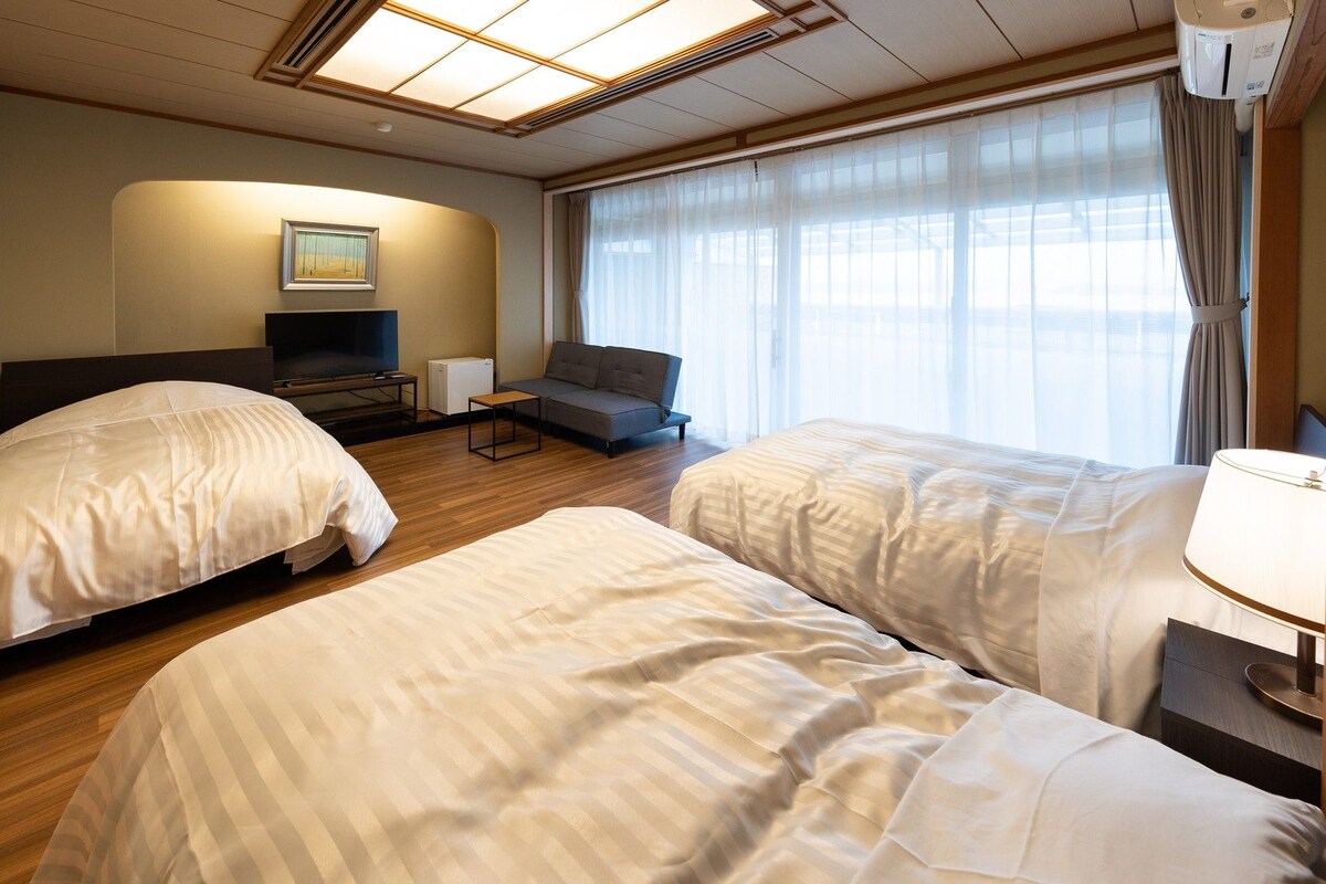 Ett hotellrum med två sängar, en soffa, en tv och ett fönster med gardiner.