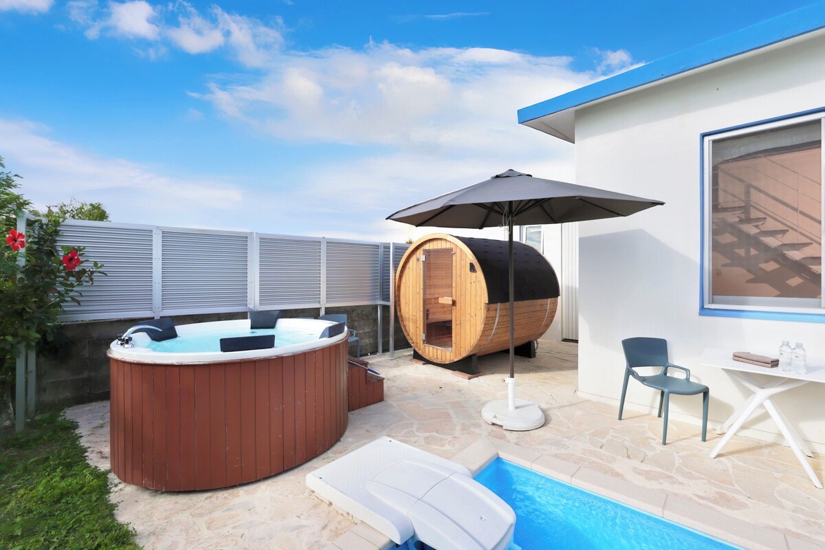 Een moderne buitenzwembadzone met een jacuzzi, een sauna en een ligstoel.