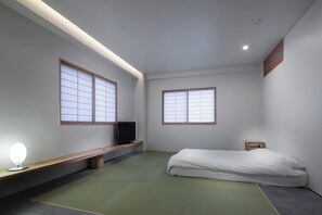 A minimalist bedroom with a bed, a bench, a TV, and two windows. - Shinjuku City Hotel N. U. T. S Tokyo (Tokyo)