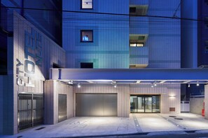 A modern building with a covered entrance, large garage doors, and a tiled facade. - Shinjuku City Hotel N. U. T. S Tokyo (Tokyo)