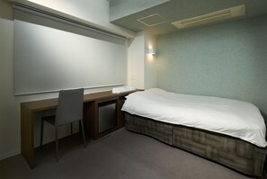 Una habitación pequeña y privada con una cama individual, un escritorio y una silla.