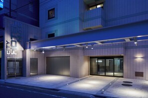 A modern hotel entrance with a covered driveway, large garage doors, and a glass entrance. - Shinjuku City Hotel N. U. T. S Tokyo (Tokyo)