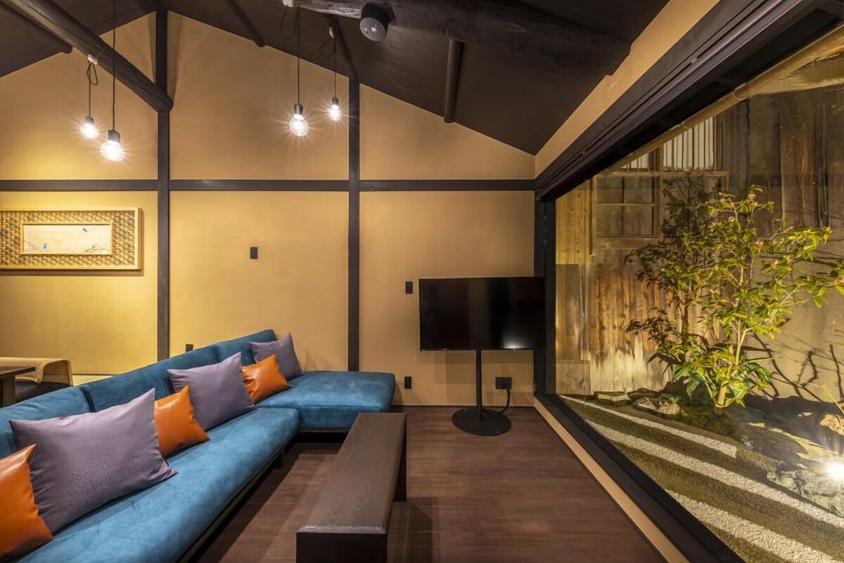 A modern living room with a blue sofa, a black floor lamp, and a large window with a view of a plant.