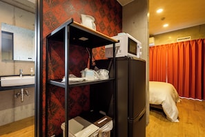 Une chambre d’hôtel équipée d’un lit, d’un four à micro-ondes, d’un lavabo et d’une étagère avec quelques objets.