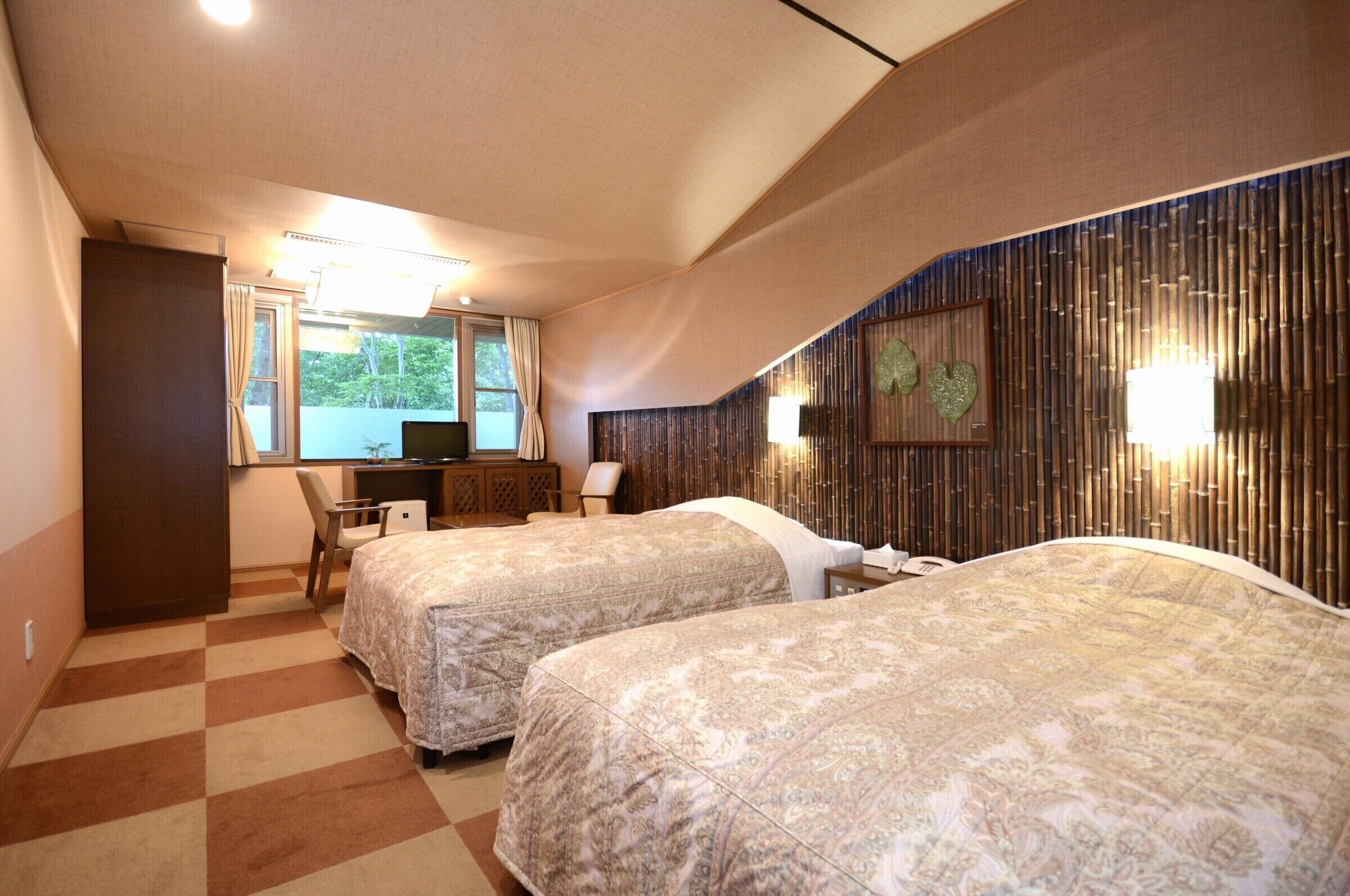 A hotel room with two beds, a desk, a chair, and a window.
