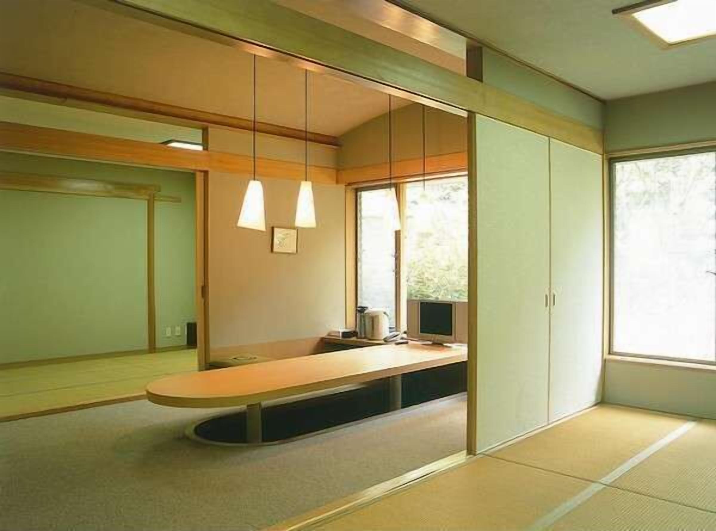 A minimalist room with tatami flooring, a low wooden desk, and a large window providing natural light.