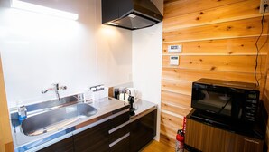A compact kitchen with a stainless steel sink, a black microwave, and a wooden wall panel. - Shioya Onsen Shioya SPA (Minakami)