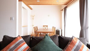 Een gezellige woonkamer met een houten plafond, een eettafel met stoelen en een bank met gestreepte kussens.