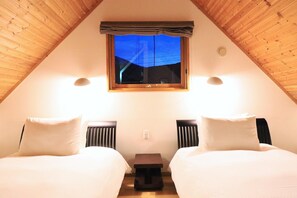 A cozy attic bedroom with two beds, a window with a view, and a small table. - Bliss Cottage Sakura (Kutchan)