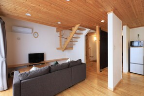 A modern living room with a wooden ceiling, a grey sofa, a flat-screen TV, and a staircase leading to another room. - Bliss Cottage Sakura (Kutchan)