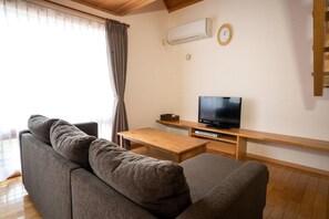 A living room with a grey sofa, a wooden coffee table, a TV on a wooden stand, and an air conditioning unit on the wall. - Bliss Cottage Sakura (Kutchan)