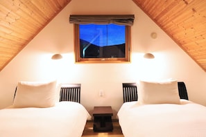 A cozy attic bedroom with two beds, a window with a view, and a small table. - Bliss Cottage Sakura (Kutchan)