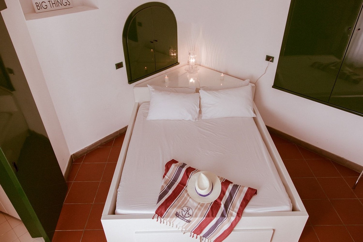 A neatly made bed with white linens, a striped towel, and a hat on the bed.