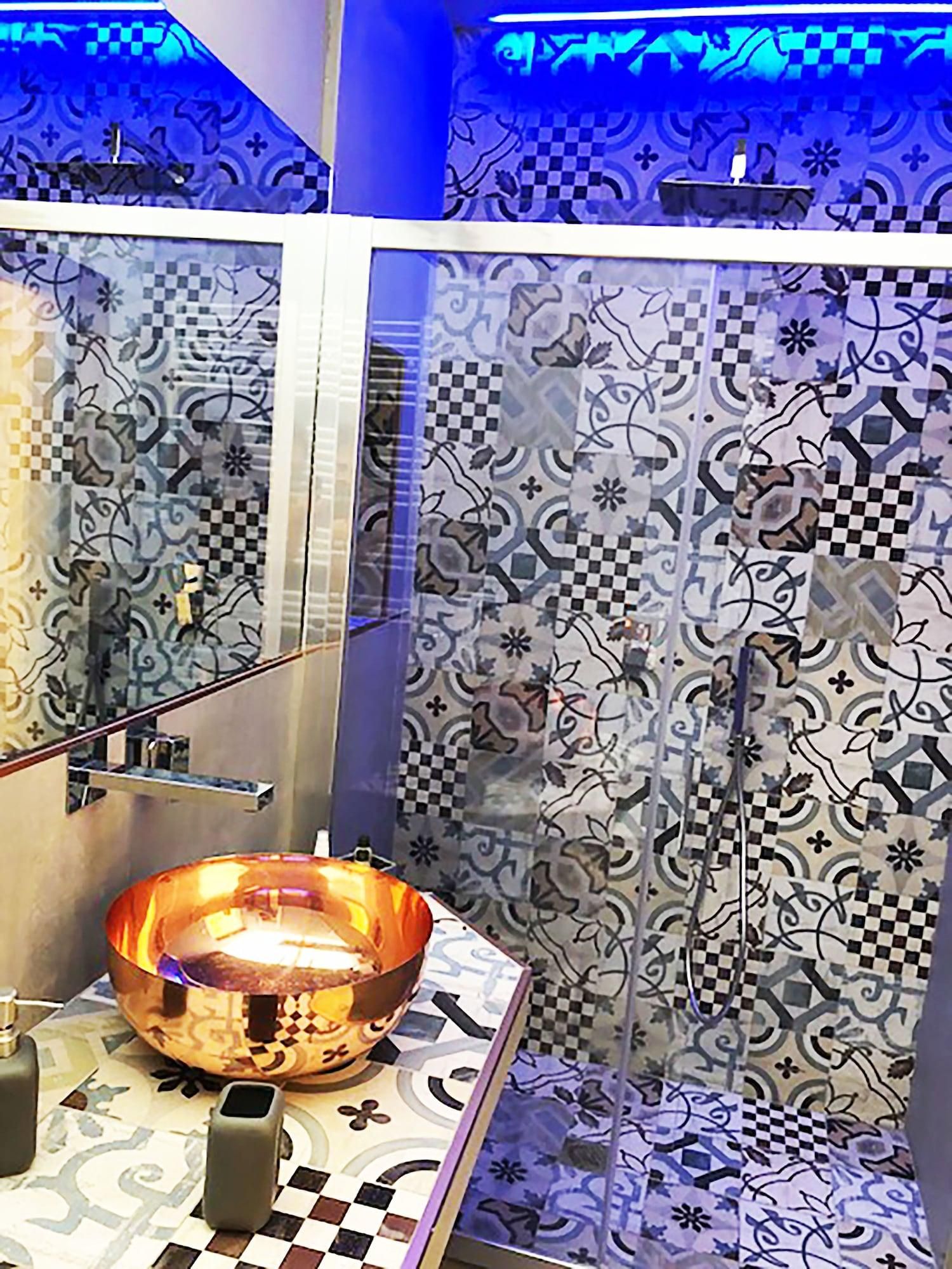 Une salle de bain avec des carreaux décorés, un lavabo en forme de bol en verre et un porte-serviettes.
