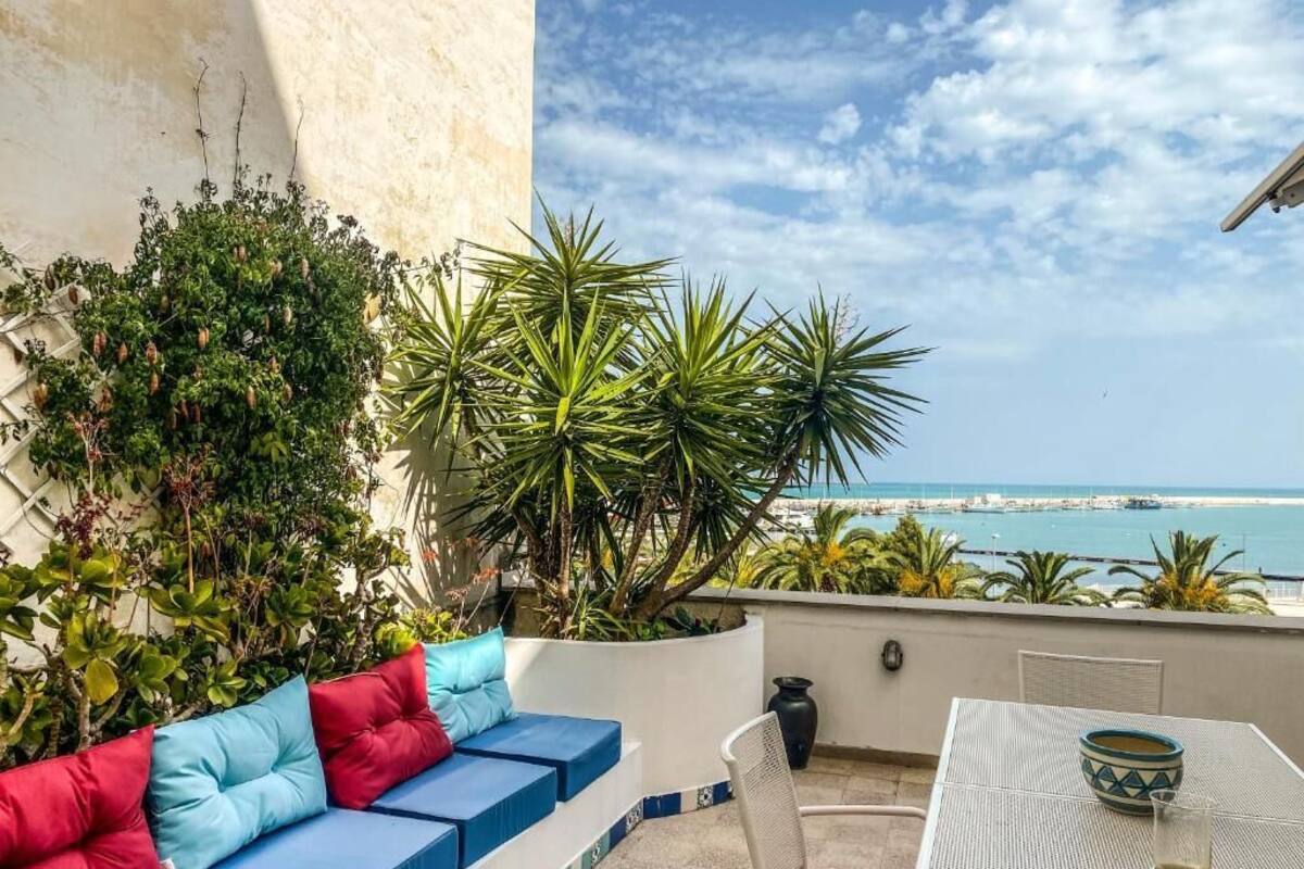 A balcony with a sofa, a table, and a view of the sea.