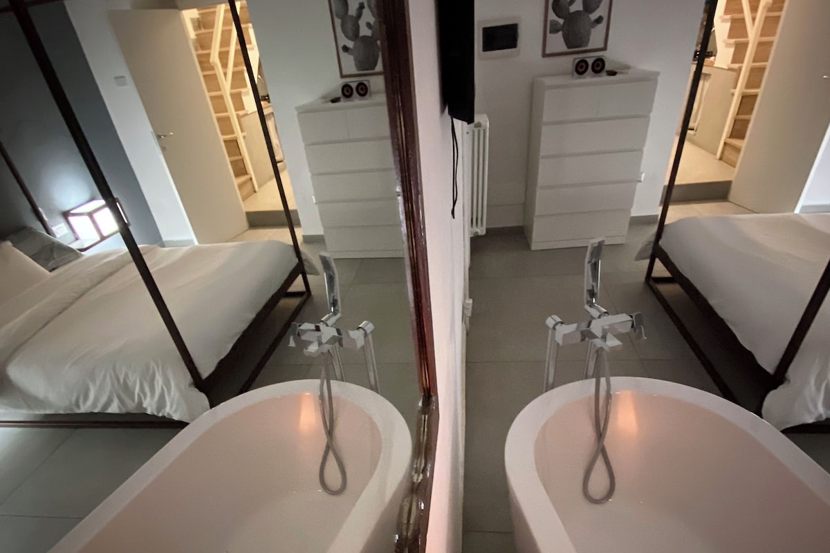 A mirrored room with two separate beds, a white bathtub, and a white dresser.