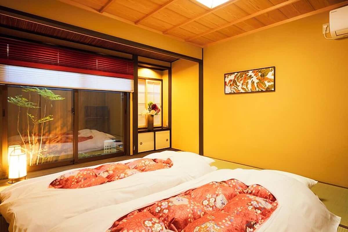 Ein Hotelzimmer mit Bett, Fenster mit Jalousien, einer Wand-Klimaanlage und einem Gemälde.
