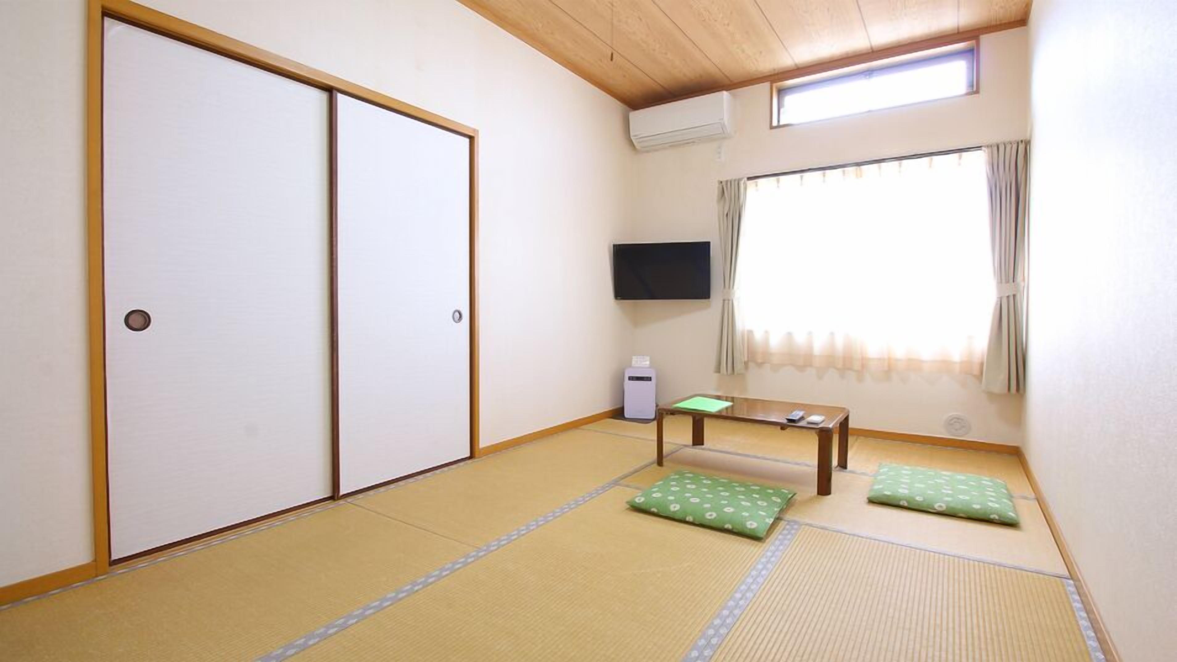 A room with tatami flooring, a sliding door, a television, a small table, and a window with curtains.