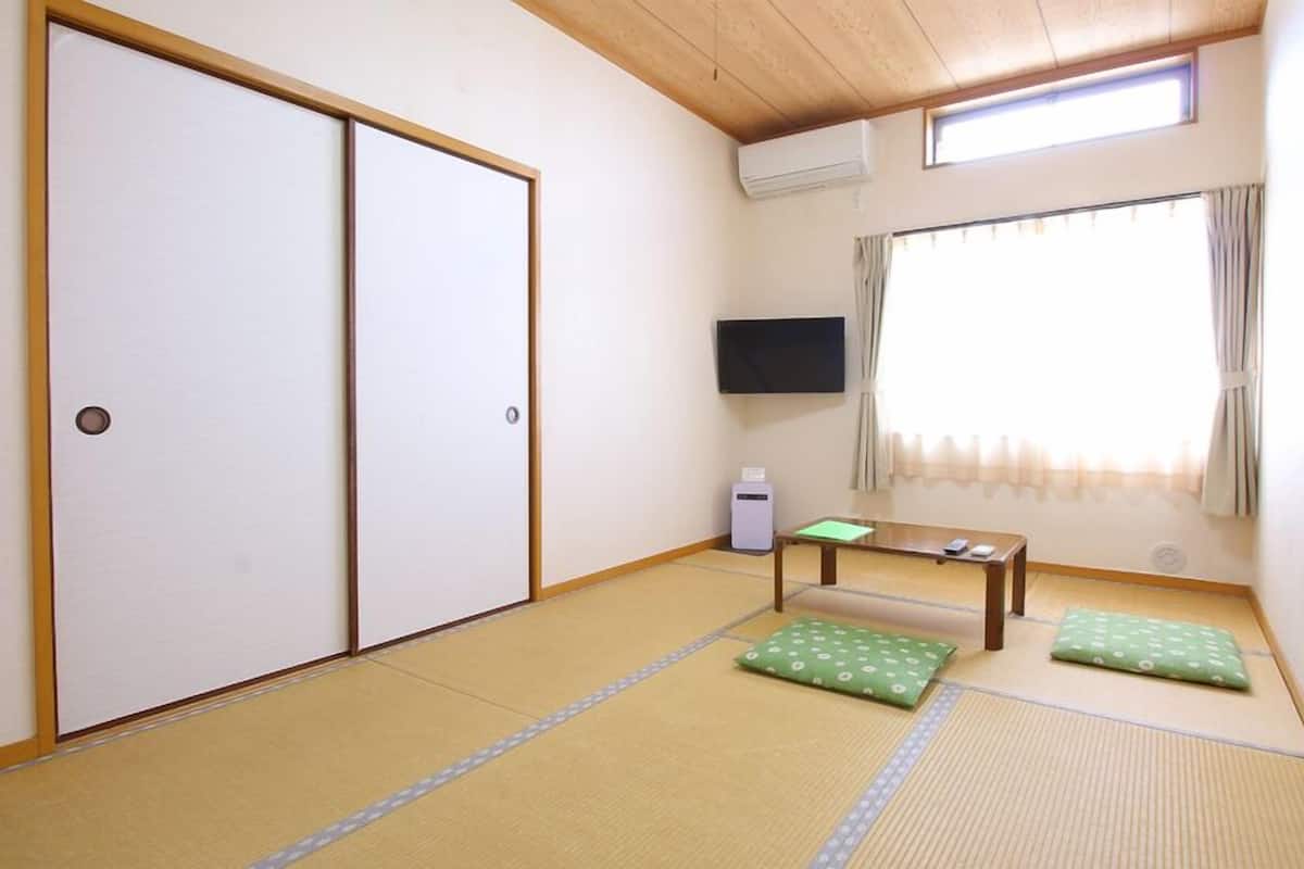 A room with tatami flooring, a sliding door, a television, a small table, and a window with curtains.