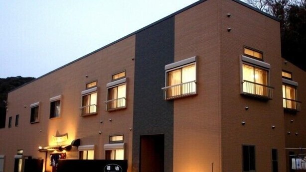 Un edificio de dos pisos con techo plano, varias ventanas y un pequeño acceso con un letrero.