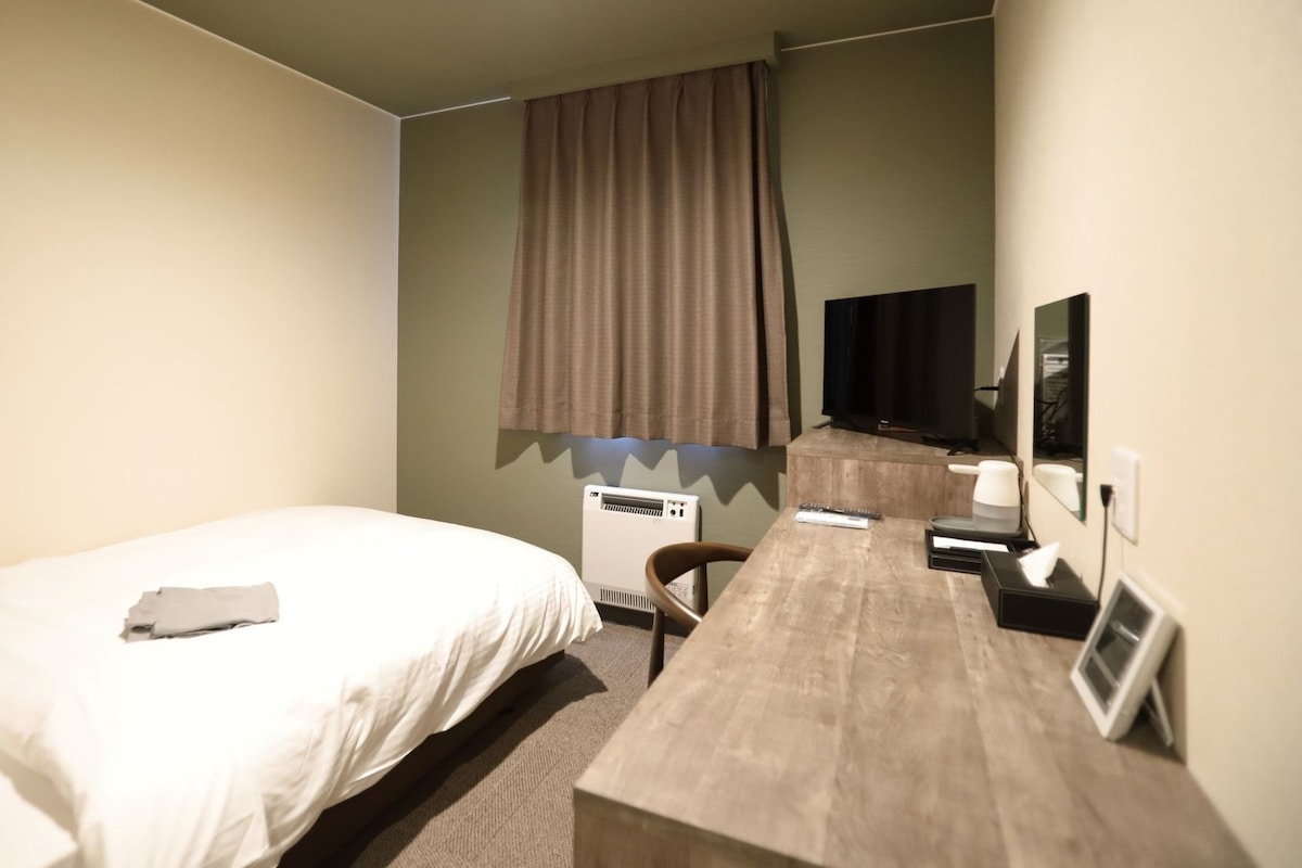 A hotel room with a bed, a desk, a chair, a television, and a window with curtains.