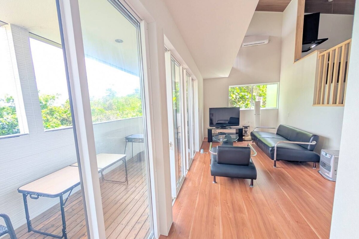 A modern living room with a TV, sofa, and a balcony with a table and chairs.