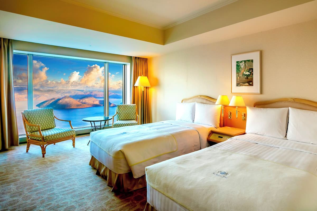 Une chambre d’hôtel avec deux lits, une chaise, une table et une grande fenêtre offrant une vue panoramique.