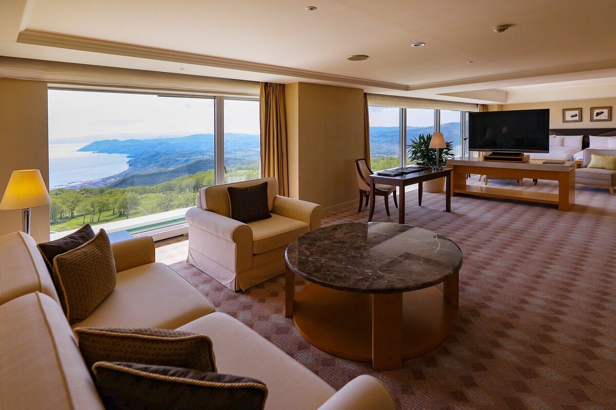 Une chambre d’hôtel dotée d’une grande fenêtre, d’un canapé, d’une table basse, d’un téléviseur et d’un coin repas.