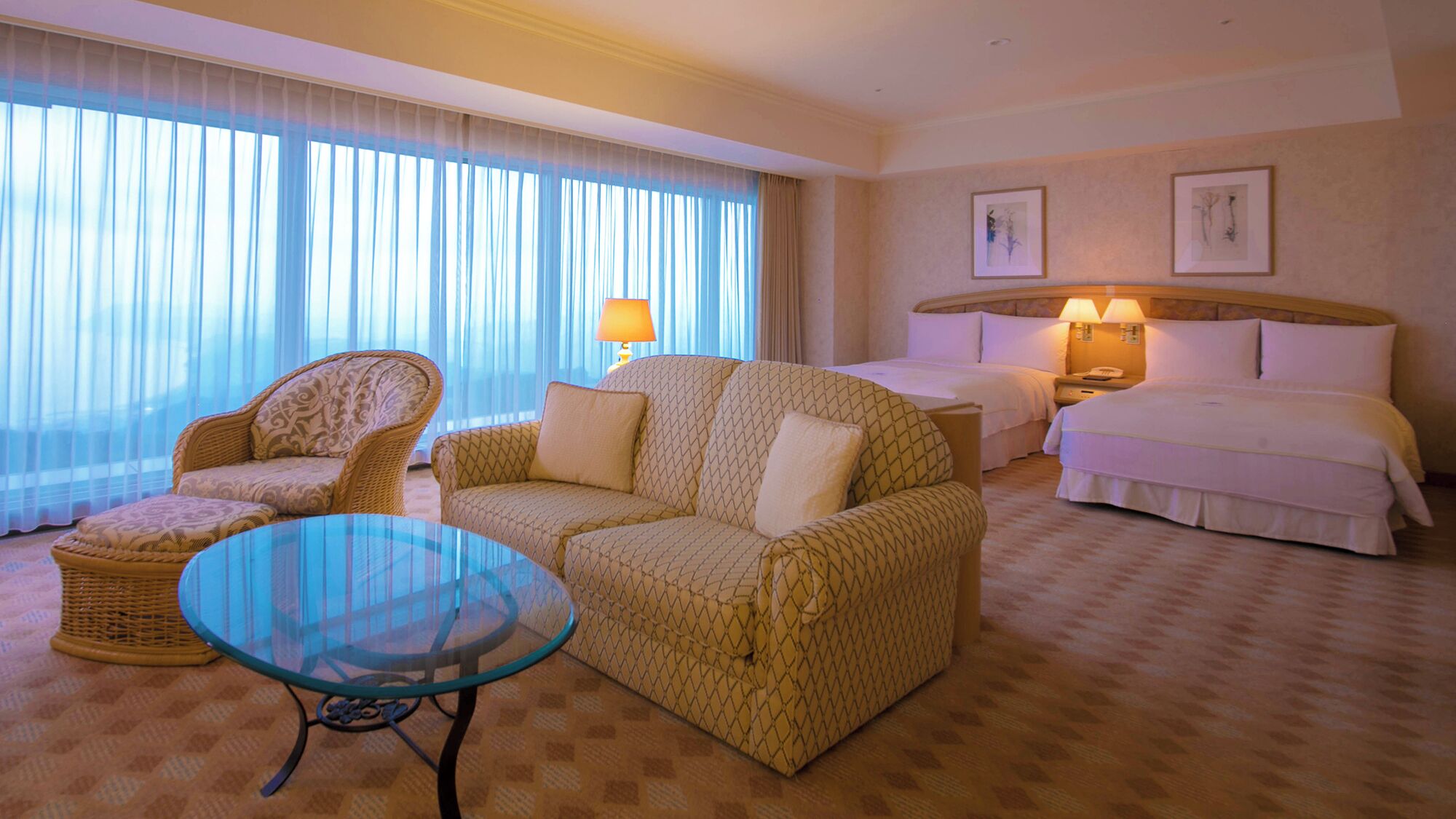 Ein Hotelzimmer mit Sofa, Glastisch, Bett, Nachttisch und Lampe.
