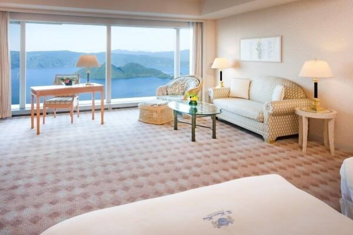 Une chambre d’hôtel avec une grande fenêtre, un lit, un canapé, une chaise et une petite table.