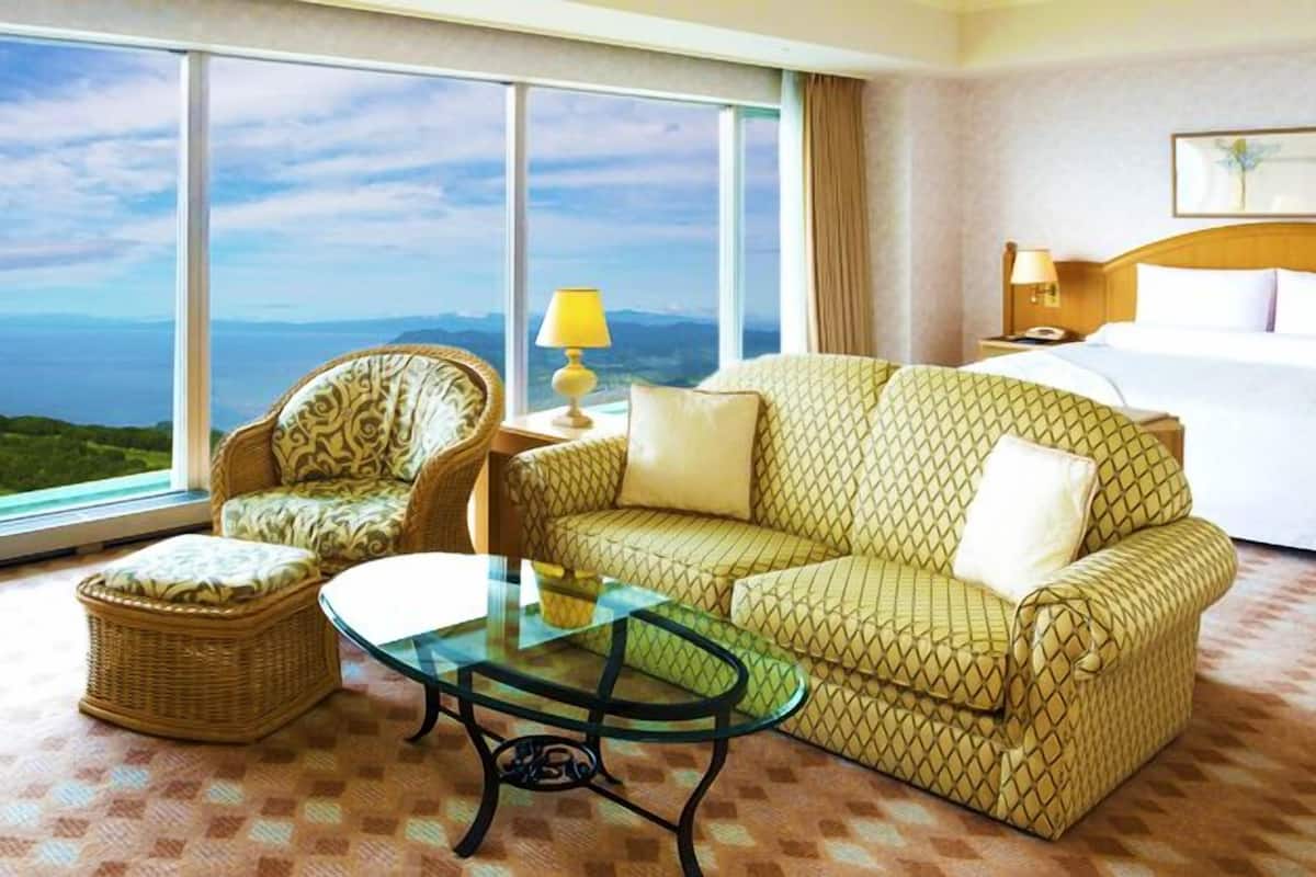 Une chambre d’hôtel avec un lit, un canapé, une chaise, une table basse en verre et une vue sur le paysage.