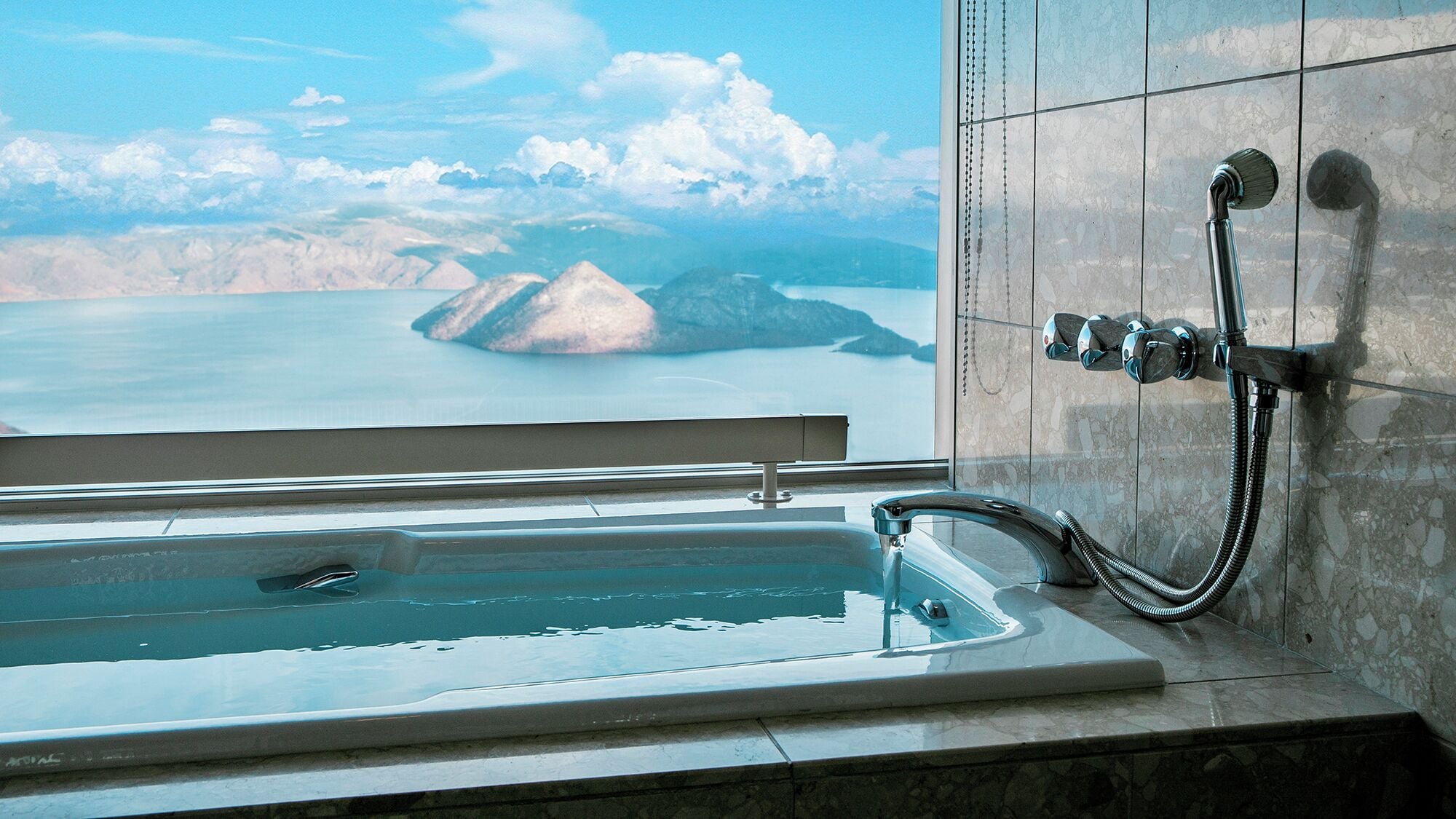 A bathroom with a bathtub, a shower, and a view of a lake and mountains.