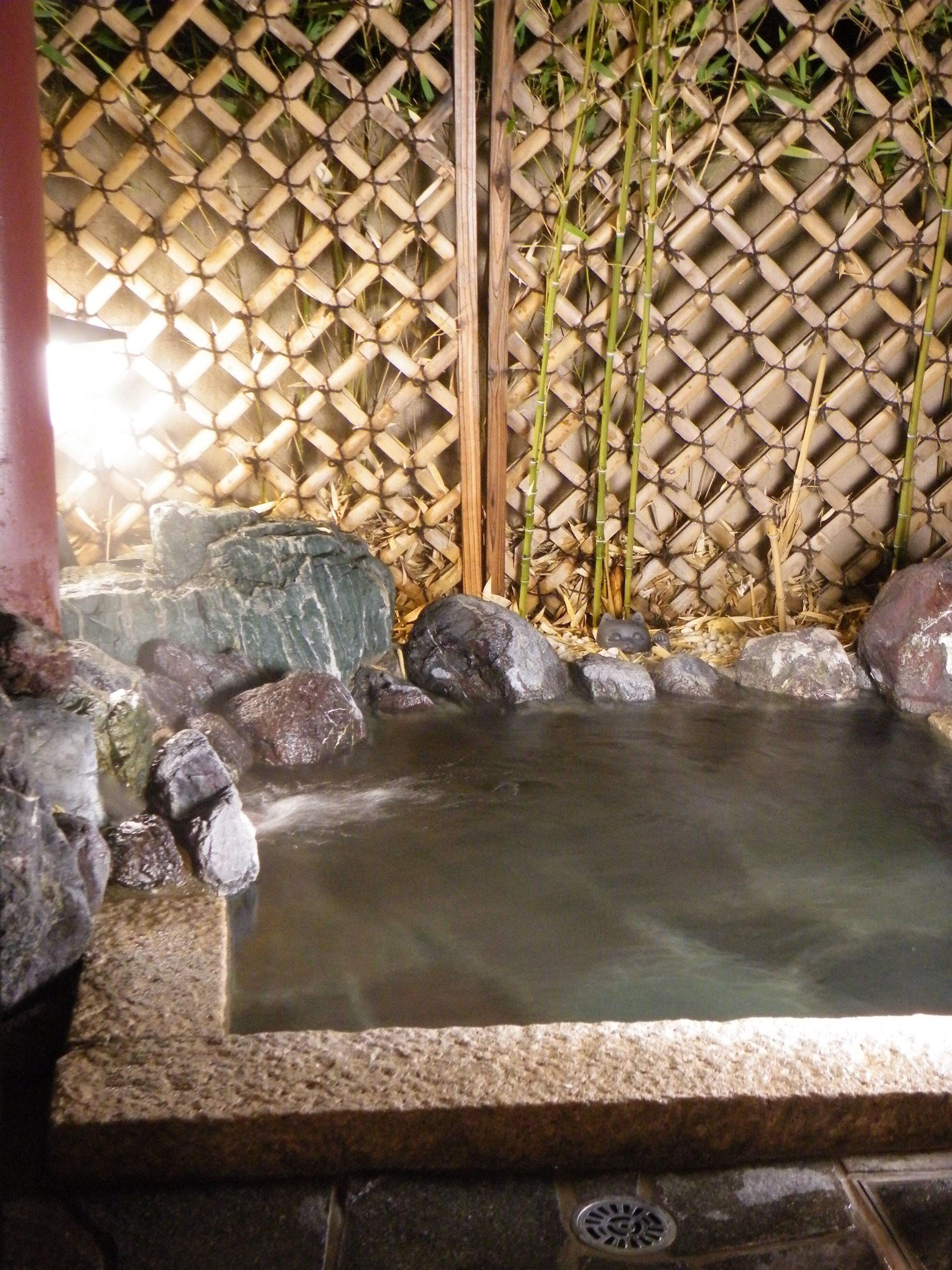 A hot spring area with a bamboo fence, rocks, and a stone basin.