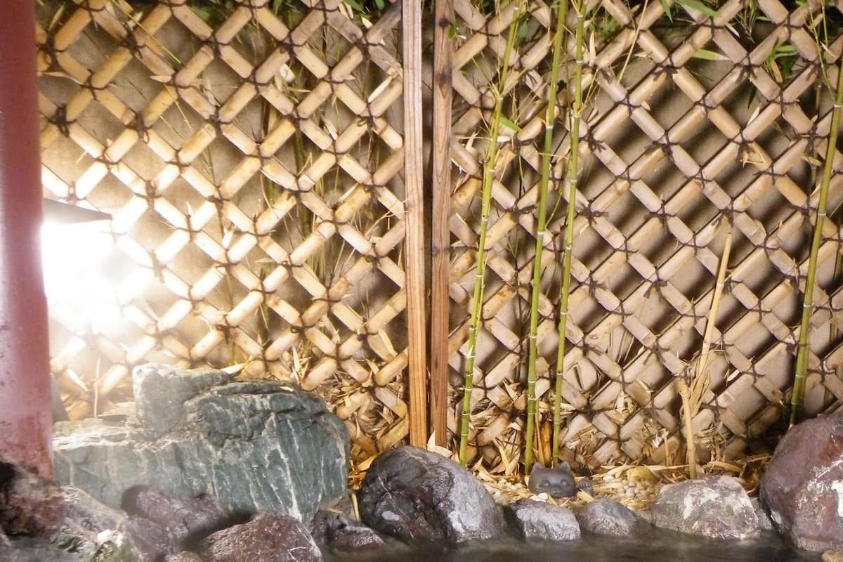 A hot spring area with a bamboo fence, rocks, and a stone basin.