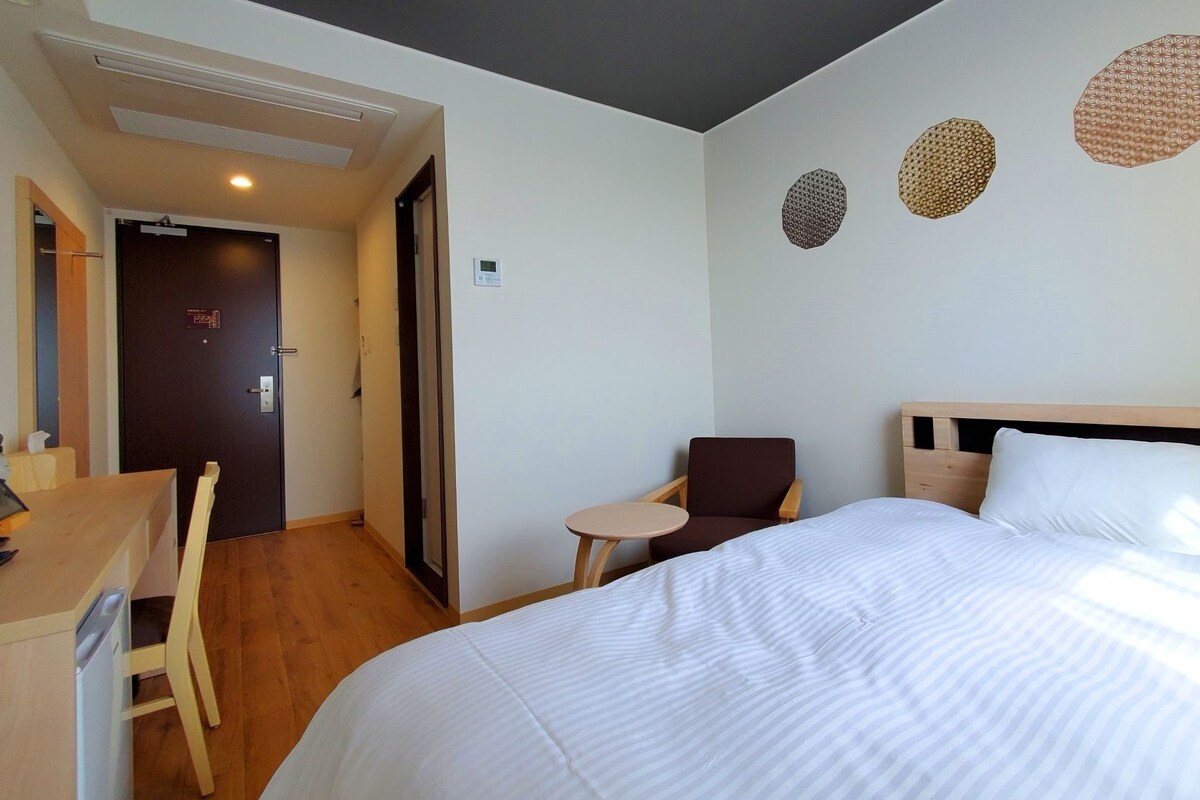 A hotel room with a bed, a desk, a chair, and a small table.