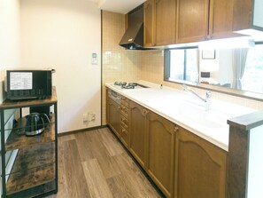 A compact kitchen with wooden cabinets, a white countertop, and a built-in stove. - Sejour Oyama Annex 3rd Building (Daisen)