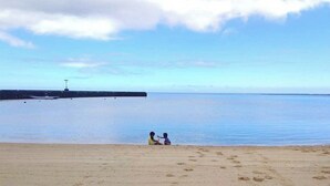 Une plage avec une jetée en arrière-plan et deux personnes assises sur le sable.