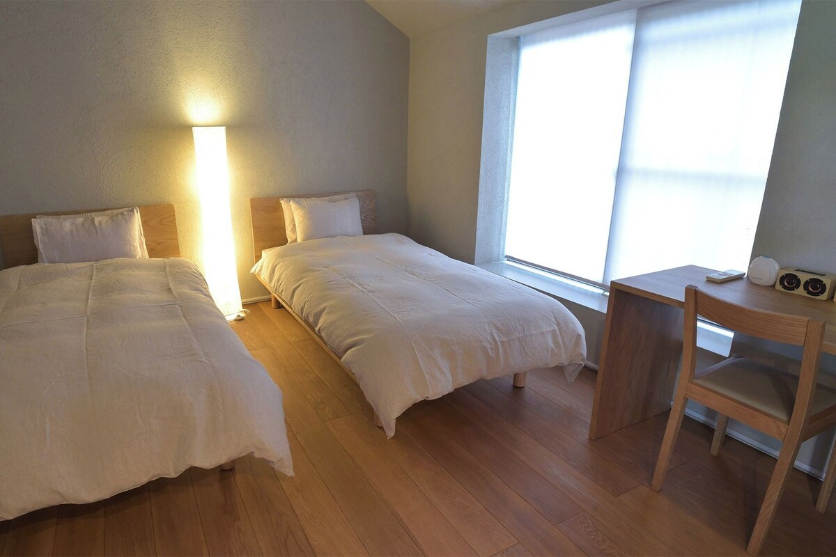 A room with two beds, a wooden desk, and a chair.