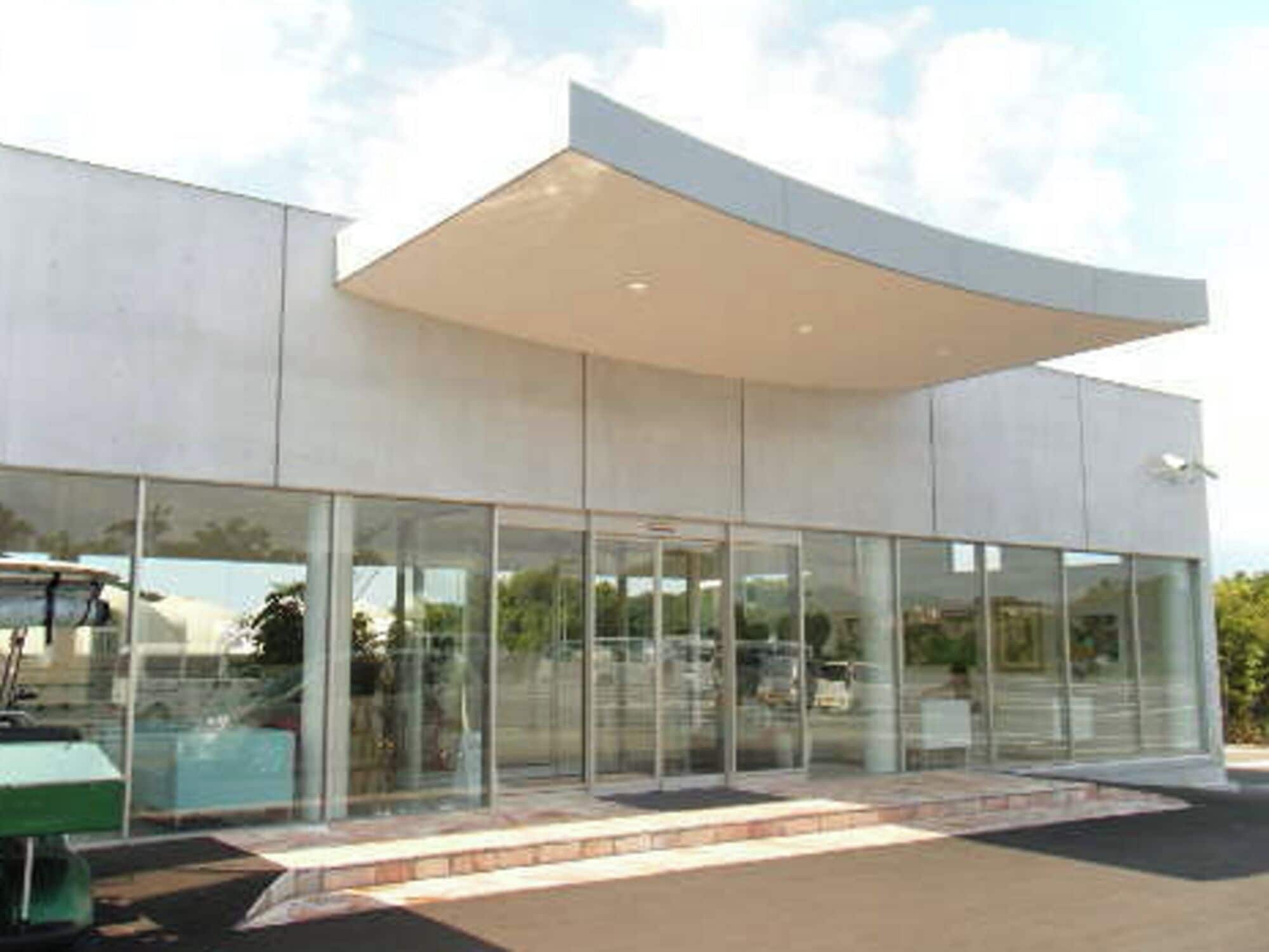 A modern building with large glass windows, a flat roof, and a paved entrance area.