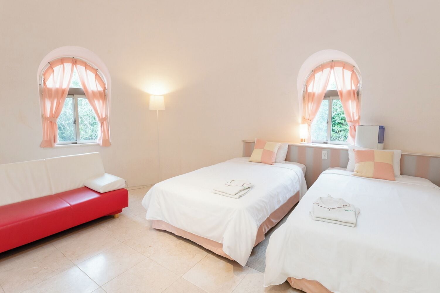A room with two beds, a red bench, and a wall-mounted lamp.