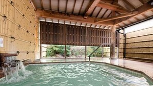 Ein Thermalbereich mit Holzbalkendecke, einem Pool und Blick ins Grüne.