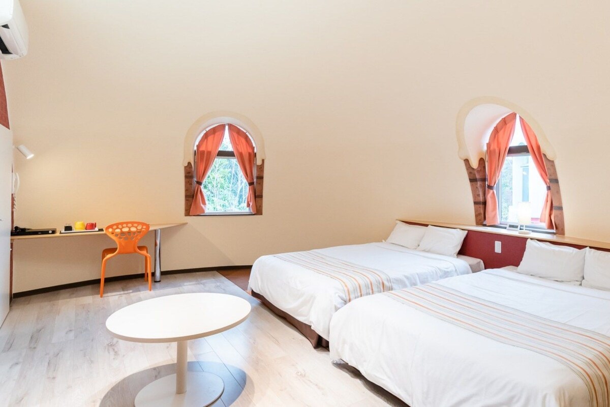 A hotel room with two beds, a desk, and two windows with curtains.