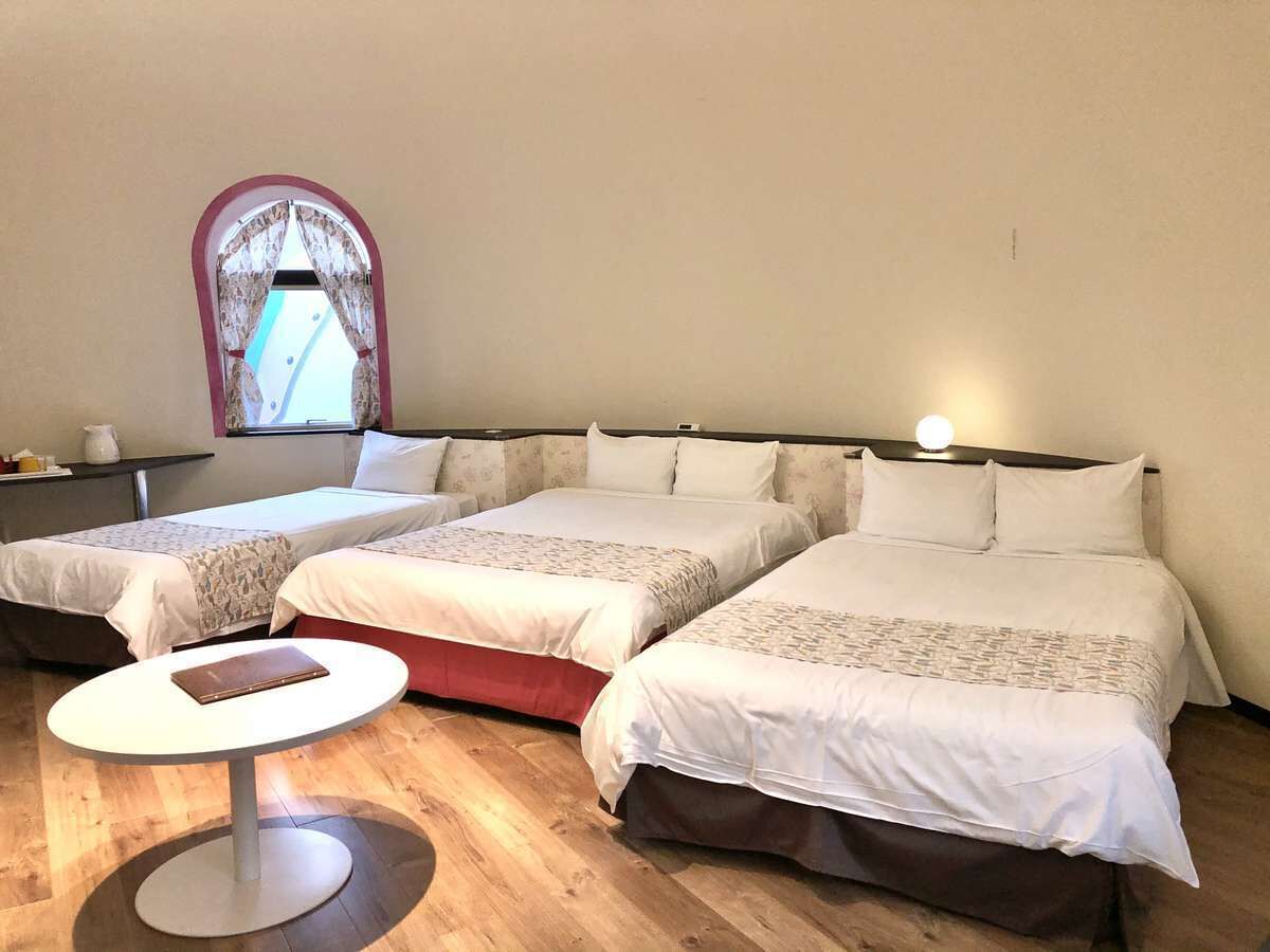 A hotel room with three beds arranged in a row, a small round table, and a window with curtains.